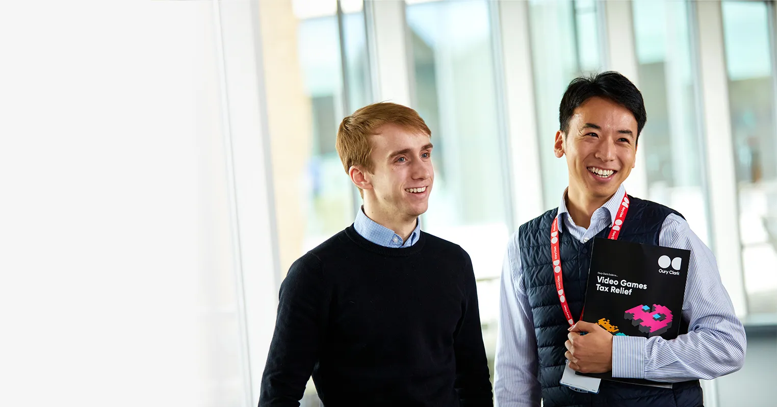 Photo of two smiling men, the one on the right is weating a lanyard and holding a copy of an Oury Clark guide to video games tax relief