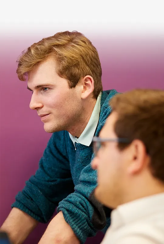 A man leans over a desk that another man sits at