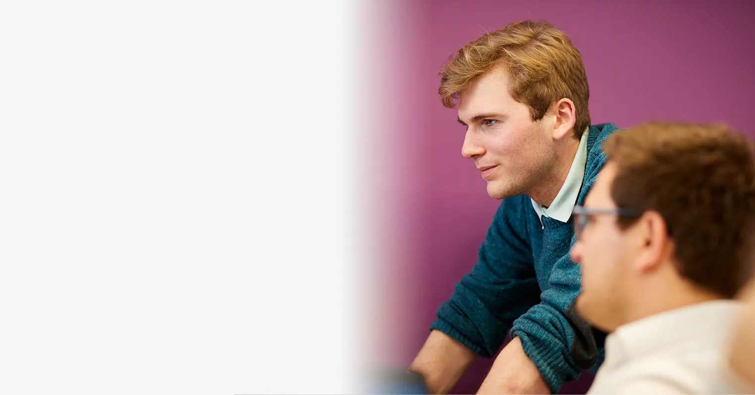 A man leans over a desk that another man sits at