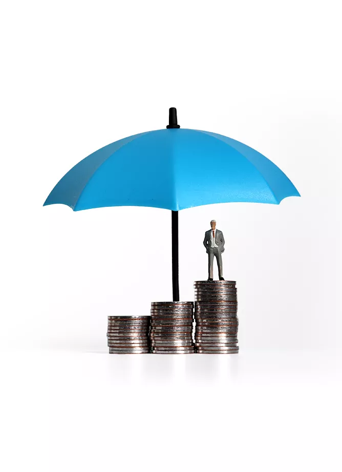 Three piles of coins, with a toy figure of a man stood on the tallest, with a blue umbrella protecting it all