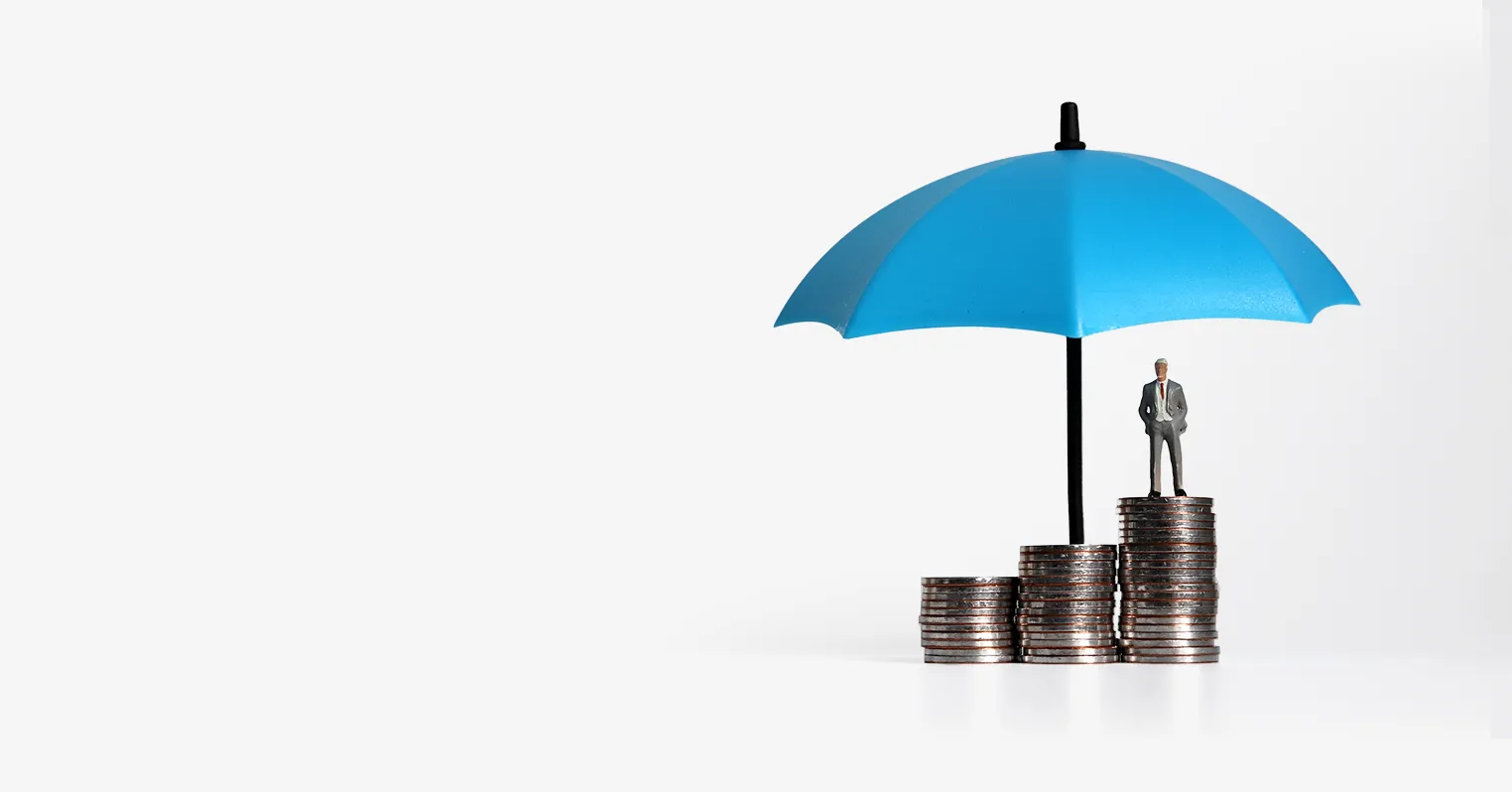 Three piles of coins, with a toy figure of a man stood on the tallest, with a blue umbrella protecting it all