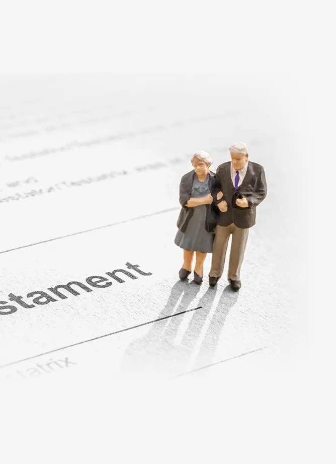 A toy figure of an elderly couple arm in arm stands on top of a legal document on which the word 'testament' can be seen